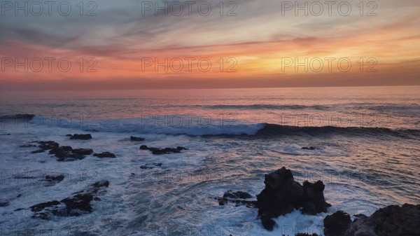 Dramatic sunset over the sea with waves crashing against black rocks, Southwest Alentejo Natural Park, Costa Vicentina, Portugal
