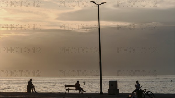 People sitting and bikers by the sea at sunset, quiet and peaceful atmosphere, waterfront, Izola, Slovenia