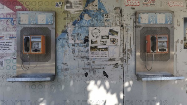 Two orange telephone boxes on a wall covered with graffiti and posters in an urban setting, Tirana, Albania