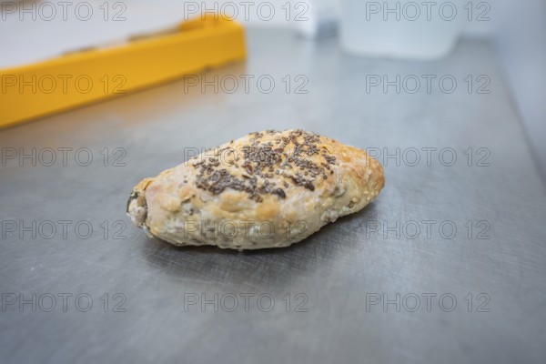 A roll with chia seeds is lying on a metal work surface in the bakery, bake rolls, Haselstaller Hof, Gechingen, Germany