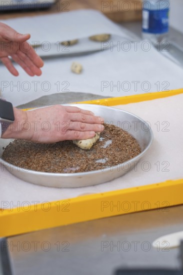 Hands press dough into a round dish filled with seeds on a yellow tray, bake rolls, Haselstaller Hof, Gechingen, Germany