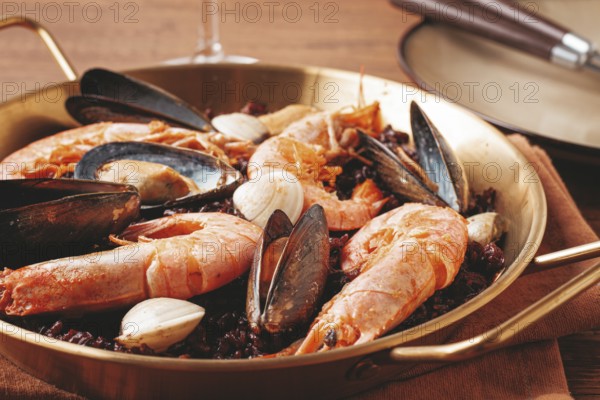 Seafood and black rice paella, in a frying pan, homemade, on a wooden table, no people