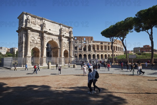 Arch of Constantine and Colosseum surrounded by tourists under blue sky and green grass, Rome, Lazio, Italy