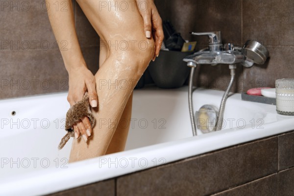 Washing slender female legs with a sponge in a bathtub. The scene captures a personal moment of self-care in the evening