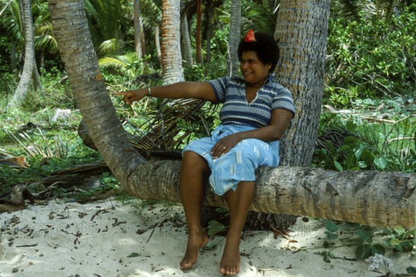 Woman sitting on a coconut trunk, (there are no chairs on Tavewa) Tavewa Island, Yasawa Islands, Fiji