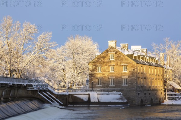 Moulin Neuf water flow control dam and walkway over Des Mille-Iles river plus New Mill on Ile des Moulins with first winter like snow in late autumn at sunset, Old Terrebonne, Quebec, Canada