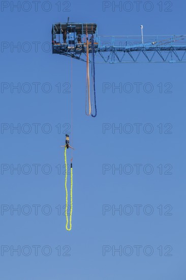 Montreal Bungee Tower installation with female bungee jumper in midair with her ankles tied to a long yellow elastic bungee jumping cord, Old Port of Montreal, Quebec, Canada