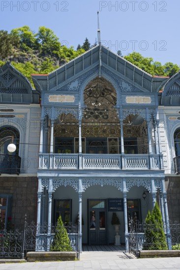 Historic blue veranda with ornate decorations and ornaments under bright sun, old villa of Mirza-Riza-Khan from the 19th century, cultural monument, Hotel Golden Tulip Borjomi, Borjomi resort, Borjomi, Kura river, Samtskhe—Javakheti region, Lesser Caucasus, Georgia