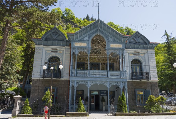 Historic blue building with abundant decorations and trees in the foreground, old villa villa of Mirza-Riza-Khan from the 19th century, cultural monument, Golden Tulip Borjomi resort, Borjomi, Kura river, Samtskhe—Javakheti region, Lesser Caucasus, Georgia
