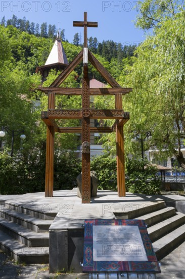 Wooden cross on a pedestal surrounded by green trees and a building, memorial to the tragedy of April 9, 1989 in Tbilisi, Borjomi resort, Borjomi, Kura river, Samtskhe—Javakheti region, Lesser Caucasus, Georgia