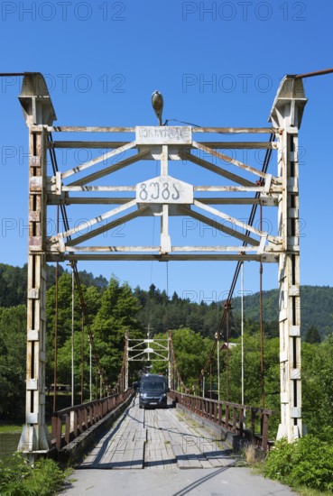 Car drives over an old suspension bridge surrounded by forest, camper, motorhome on a suspension bridge across the Kura River near Kortaneti, Samtskhe—Javakheti region, Georgia