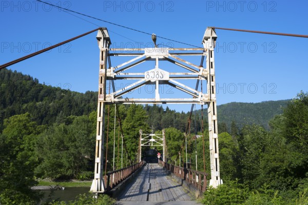 Steel bridge crosses a river amidst forested mountains, suspension bridge across the Kura River near Kortaneti, Samtskhe—Javakheti region, Georgia