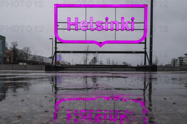 Large pink glowing city logo of Helsinki, in front of Oodi Central Library and Cultural Center, reflected on wet ground, Helsinki, Finland