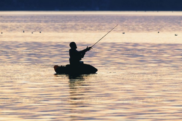 Angler sport fisherman in his belly boat in orange-red lake at sunset, silhouette in calm water, relaxed atmosphere, Lembruch, Dümmer See, Lower Saxony, Germany