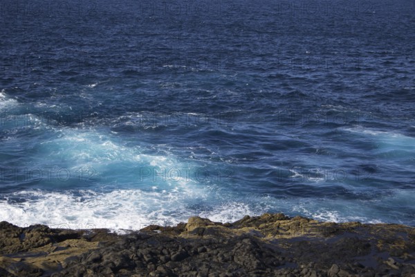 Waves break on a rocky coastline under deep blue skies, Yaiza Lanzarote