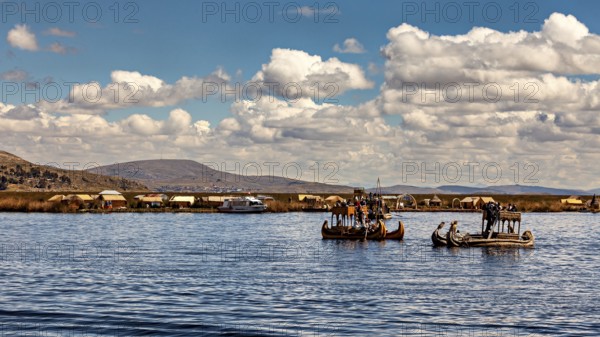 Traditional reed boats on a lake with a village on the shore under blue skies, The floating reed islands of the Uros in Lake Titicaca in Peru