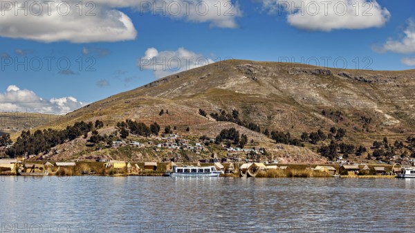 View of a lakeside village with hills in the background and clouds in the sky, The floating reed islands of the Uros in Lake Titicaca in Peru