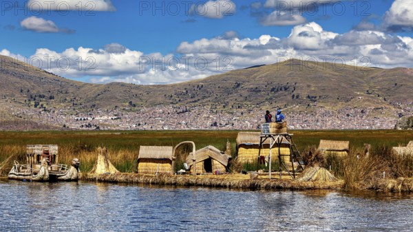Reed huts and lakeside observation tower in sunny weather with mountains in the background, The floating reed islands of the Uros in Lake Titicaca in Peru