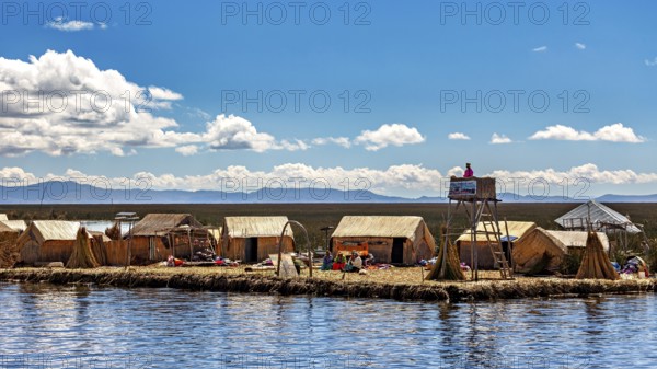 Reed huts and people on an island under a partly cloudy sky with a wide landscape, The floating reed islands of the Uros in Lake Titicaca in Peru