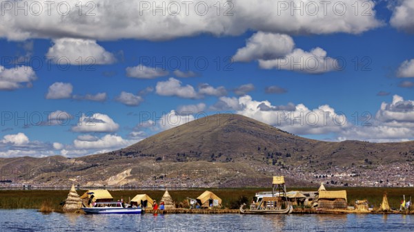Reed village on the shore of a lake with big mountains in the background under a cloudy sky, The floating reed islands of the Uros in Lake Titicaca in Peru