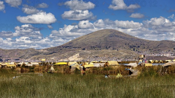 Islands surrounded by reeds and mountains under a cloudy sky in a peaceful landscape, The floating reed islands of the Uros in Lake Titicaca in Peru