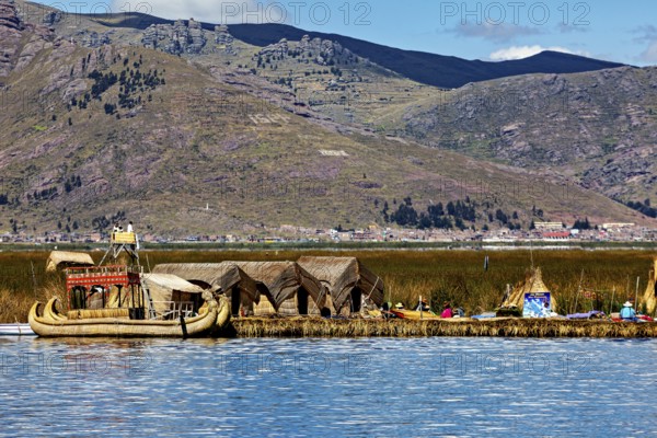 Reed boats and huts on a lake with mountains in the background, The floating reed islands of the Uros in Lake Titicaca in Peru