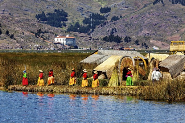 Women in traditional clothing in front of reed huts on an island in the lake, The floating reed islands of the Uros in Lake Titicaca in Peru
