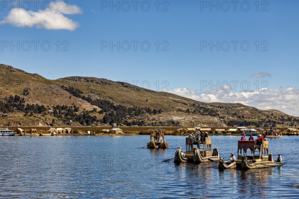 Traditional boats and people on a lake with a sweeping view of the shore, The floating reed islands of the Uros in Lake Titicaca in Peru