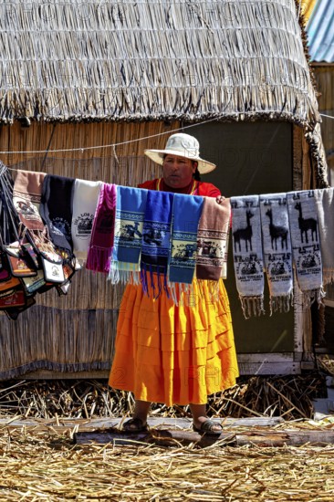 Woman showing colorful, handmade cloths in front of a thatched hut, The floating reed islands of Uros in Lake Titicaca in Peru
