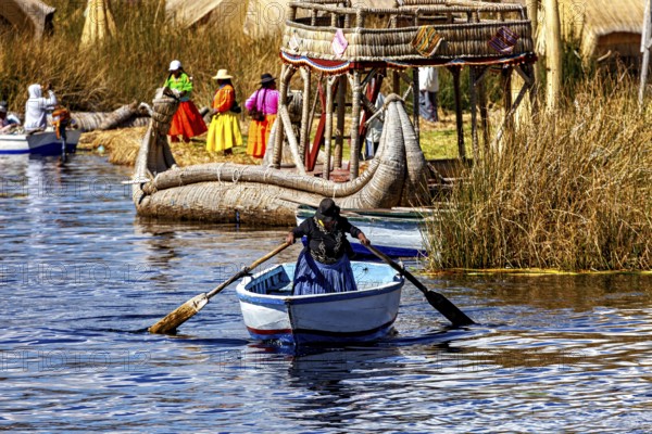 A woman rows in a waterway between large reed canoes and village life, The floating reed islands of the Uros in Lake Titicaca in Peru
