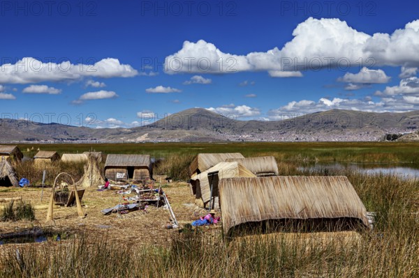A village with reed huts on a lake under a cloudy blue sky, The floating reed islands of the Uros in Lake Titicaca in Peru