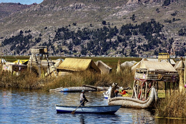 A boat sails on a lake against a backdrop of reed huts and mountains, the floating reed islands of the Uros in Lake Titicaca in Peru