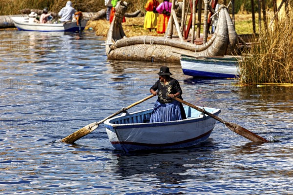 A woman in traditional dress rows a boat across a calm lake, the floating reed islands of the Uros in Lake Titicaca in Peru