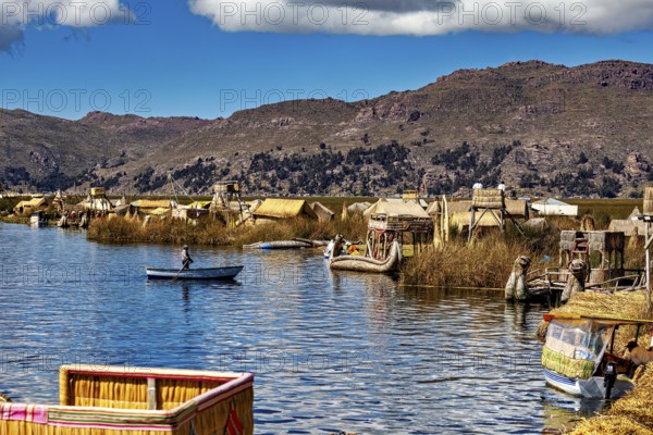 Canoe on a lake with traditionally built reed huts and mountains, The floating reed islands of the Uros in Lake Titicaca in Peru