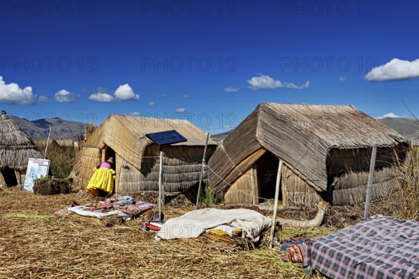 Reed huts with solar panels under a clear blue lakeside sky, The floating reed islands of the Uros in Lake Titicaca in Peru