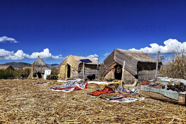 Straw huts on an island with traditional handmade objects in the foreground, The floating reed islands of the Uros in Lake Titicaca in Peru