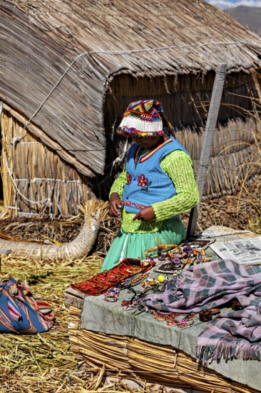 Woman in colorful traditional clothing in front of a reed hut with handmade objects, The floating reed islands of the Uros in Lake Titicaca in Peru