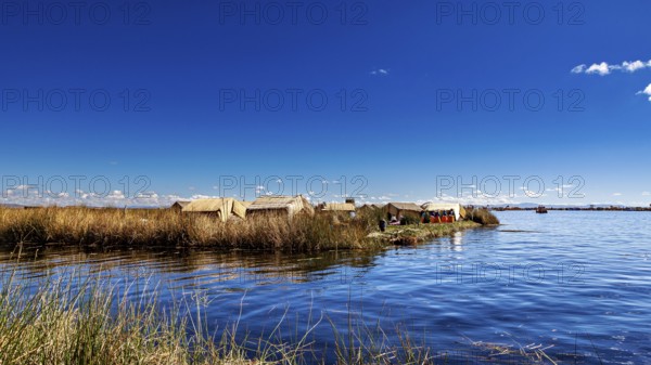 View of reed huts on the coast of a lake under expansive blue sky, The floating reed islands of the Uros in Lake Titicaca in Peru