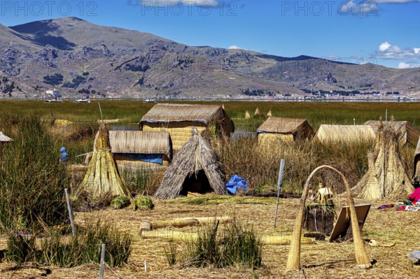 Traditional reed huts on the edge of a lake with mountains in the background, The floating reed islands of the Uros in Lake Titicaca in Peru