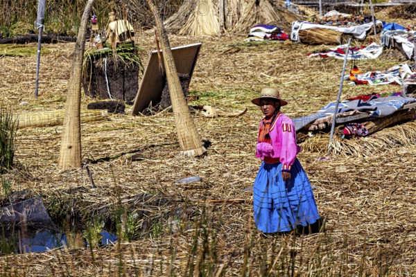 A woman in traditional dress stands in a quiet village made of reeds, The floating reed islands of the Uros in Lake Titicaca in Peru