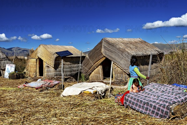 Woman approaches huts made of reeds, dressed in traditional clothing, The floating reed islands of the Uros in Lake Titicaca in Peru