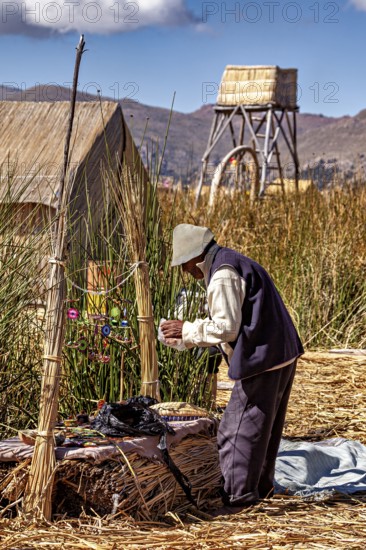 Man is engaged in handicraft work next to traditional reed huts, the floating reed islands of the Uros in Lake Titicaca in Peru