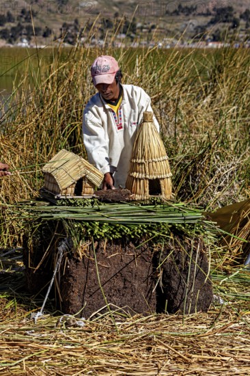 Man showing a model of straw huts and figures on a natural surface, The floating reed islands of the Uros in Lake Titicaca in Peru