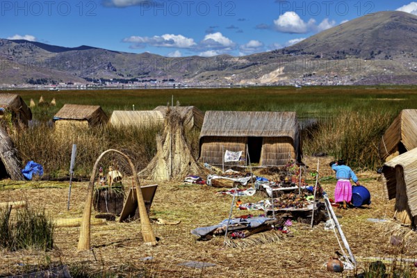 Reed huts with mountains in the background and scattered crafts, The floating reed islands of the Uros in Lake Titicaca in Peru