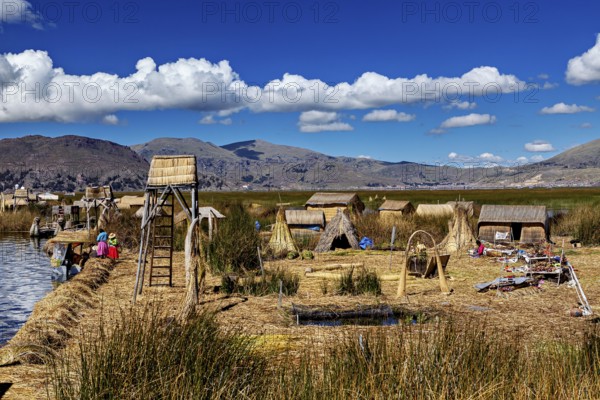 A traditional village with reed huts and views of mountains under cloudy skies, The floating reed islands of the Uros in Lake Titicaca in Peru