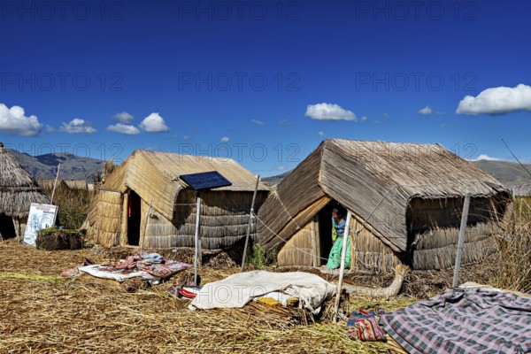 Several reed huts with solar panels under a blue lakeside sky, The floating reed islands of the Uros in Lake Titicaca in Peru