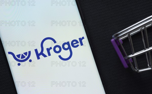 Dhaka, Bangladesh- 03 July 2025: A smartphone displaying the Kroger logo next to a miniature shopping cart on a background