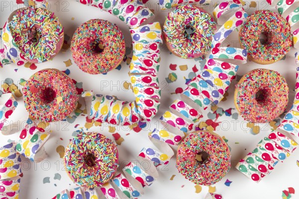 Donuts with colorful icing surrounded by confetti and streamers on a white background, carnival