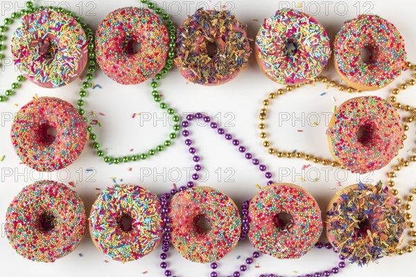 Donuts with colorful icing and sprinkles surrounded by colored pearl necklaces on a white background
