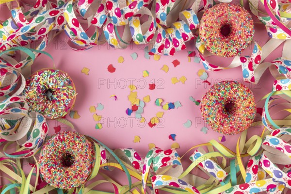 Donuts, streamers and scattered confetti on a pink background, Mardi Gras